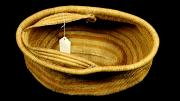 An open, oval shaped, single handled basket with yellow vegetable dye stripes.