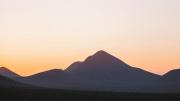 "A photograph of a mountain with the sun rising behind it."
