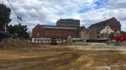 Flat ground with sand on it, heritage buildings in the background, cloudy sky 