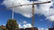 A yellow crane sites above a heritage building.  Big white clouds are behind in a blue sky. 