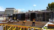 Five workers in high vi vests and hard hats bend over and attach reinforced steel together 