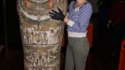 A woman standing next to an upright sarcophagus
