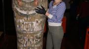 A woman standing next to an upright sarcophagus