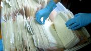 Image of a person's hands going through a box filled with badges in clear plastic bags. 