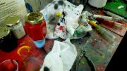 Image of a table covered in paints, syringes, cloths and other tools used for colouring badges. 