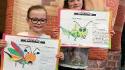 "Two children stand showing off artworks they have created."