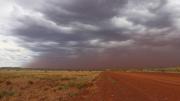 A red storm cloud over a flat grassy landscape with a gravel road