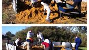 workers use shovels and a wheelbarrow to shift yellow sand out of the way