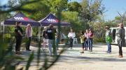 "Through a branch in the foreground a group of adults and children can be standing in a carpark in front of marquees with the WAM Logo on them."