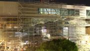 A large building covered in scaffolding glows with golden lights at night.