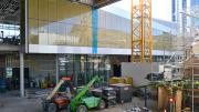 Large scale construction equipment sits on a dirt floor surrounded by glass walls and an uncovered steel roof.