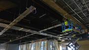 Man on scissor lift works on the ceiling of a large room with industrial roof.