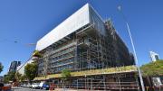 A large building with scaffolding around it and a white finish to the very top floor.