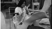 A woman sits on a chair inspecting a large whale bone in front of her.