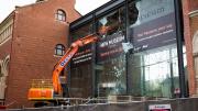 An orange construction machine with a crane arm taps the glass of the foyer which is smashing. 