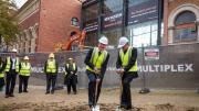 Two men in high vis vests hold shovels ready to ceremonially dig up earth (turning the first sod)