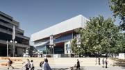 A large building sits on the horizon line of a public square where people sit.