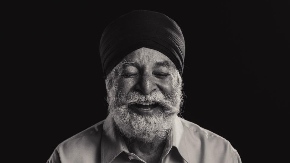 "Man with silver beard wearing turban laughs, his eyes are closed."