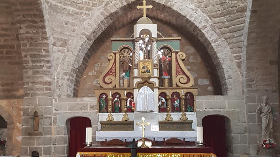 "Chapel with religious cross and alter with yellow and white fabric within a stone building."