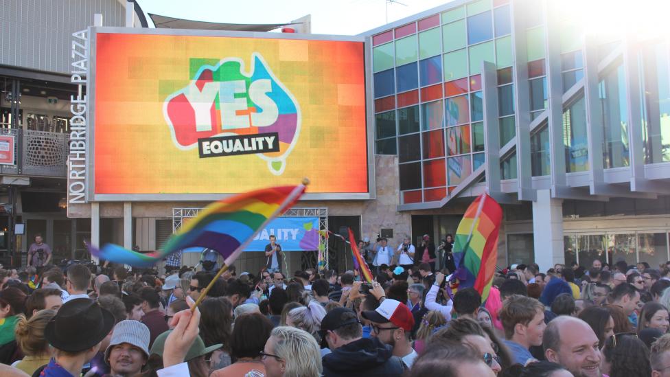 People celebrate the Yes vote, waving LGBQTI flags and a large screen in the background has YES displayed