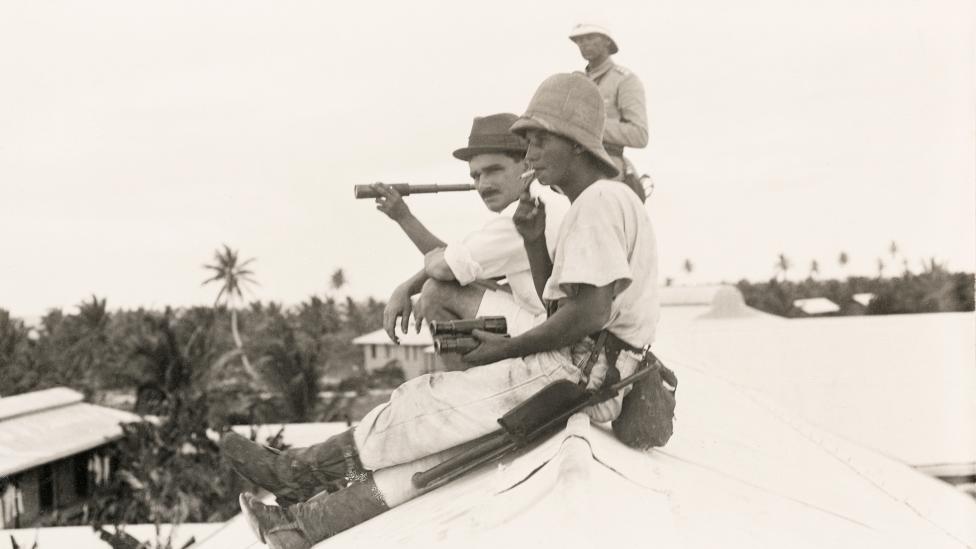 Two people sitting on a roof top watching a naval battle