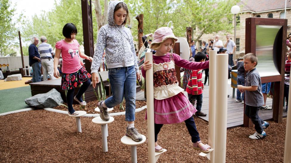 Children walking on stilt-like equipment in a play space 