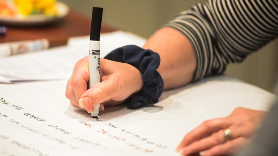 A woman's hand holding a pen writing on a large piece of paper.