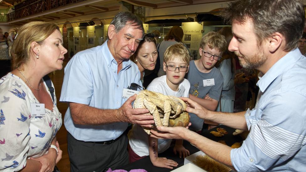 Curator handing a shell to a man, woman to his left and children to his right.