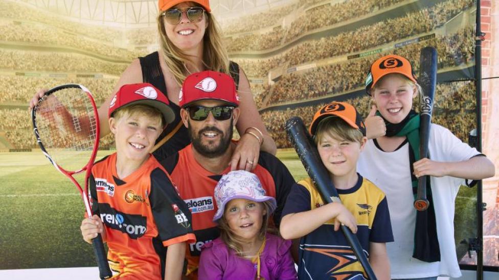 "A Mum and Dad are surrounded by their four children. Everyone is wearing sporting gear with tennis rackets."