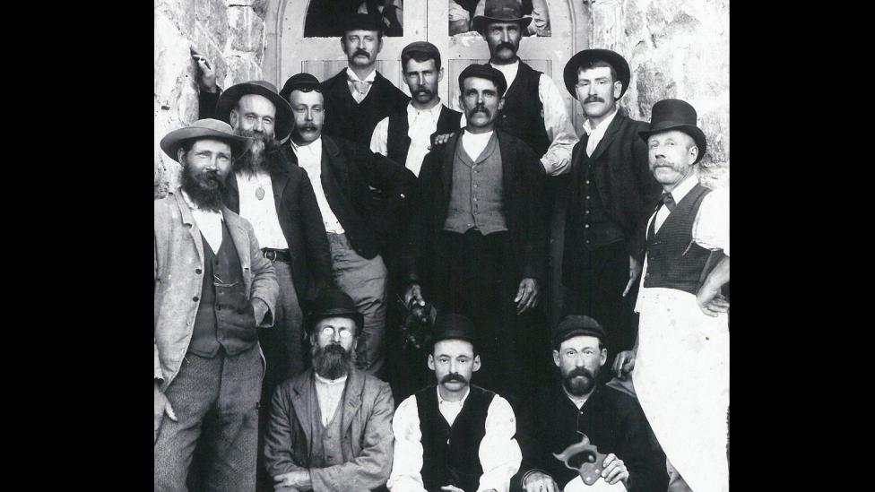 A group of builders wearing 19th century style clothing standing in front of a court house