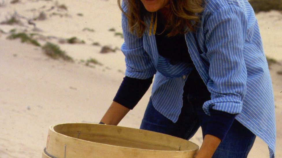 "A woman is sifting through sand during an archaeological dig."