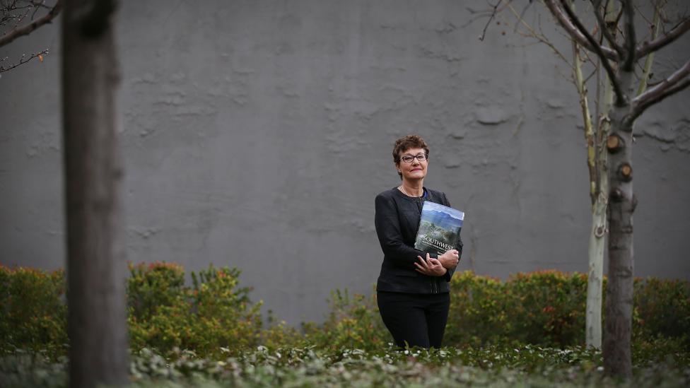 A woman standing in a garden holding a book.