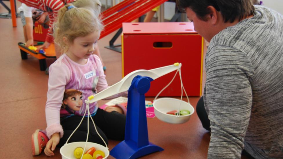 "A child and guardian are experimenting with different weights on a scale."