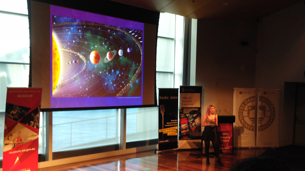"A young presenter standing in front of a screen with a planet powerpoint."