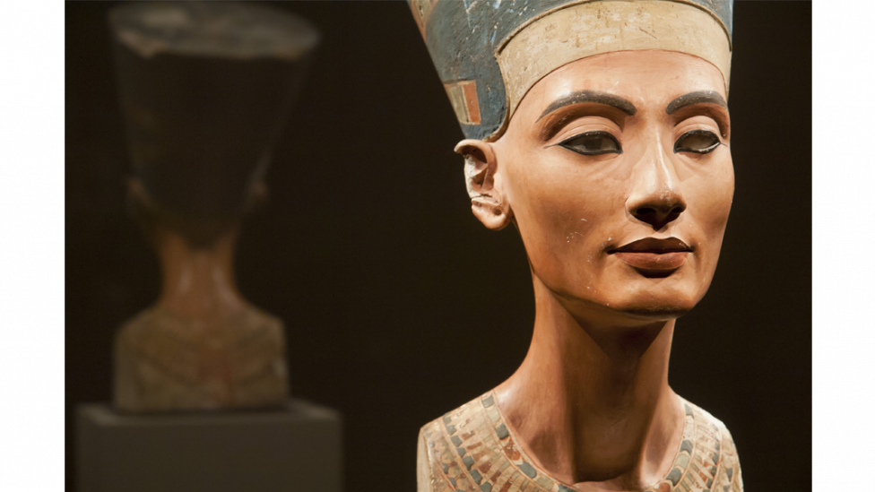 "A coloured bust sculpture of Nefertiti in a museum display cabinet."