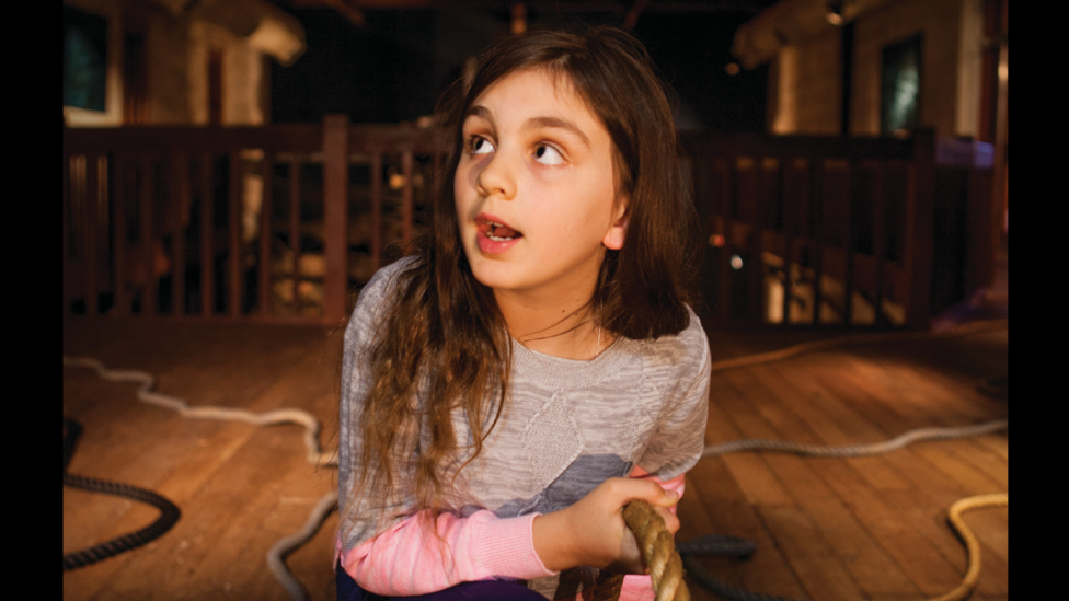 "A girl is looking around the Museum while holding one of many ropes."