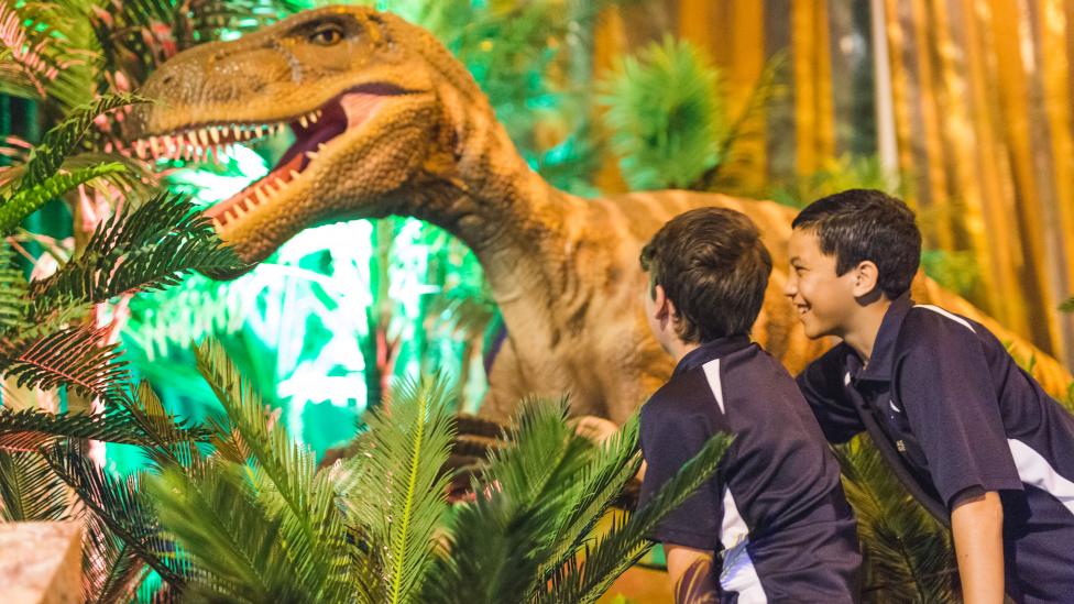 "Two young boys are touching the claw of an animatronic dinosaur."