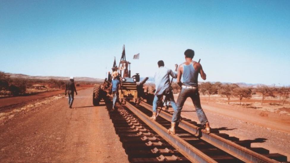 "A group of men are laying a railroad track in the outback."