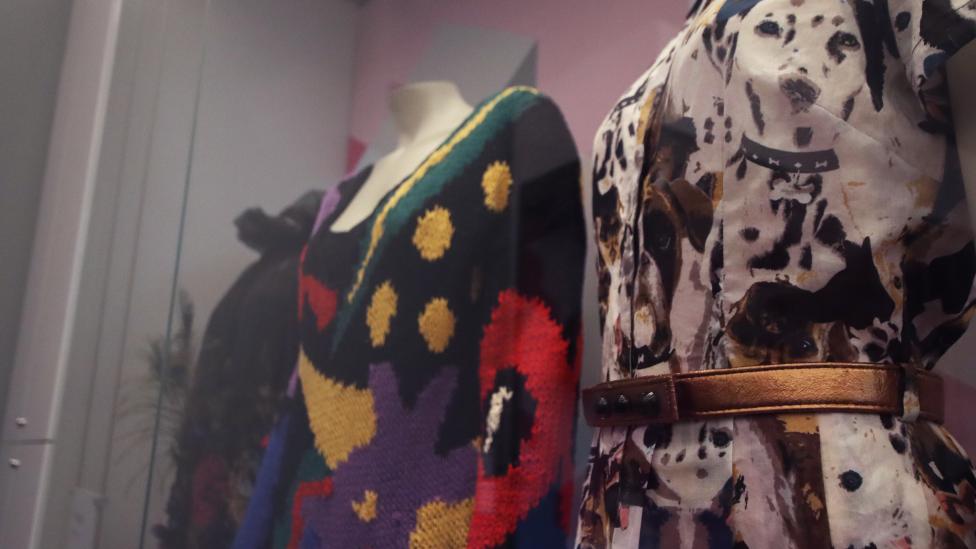 Three dresses are displayed on mannequins in a museum showcase