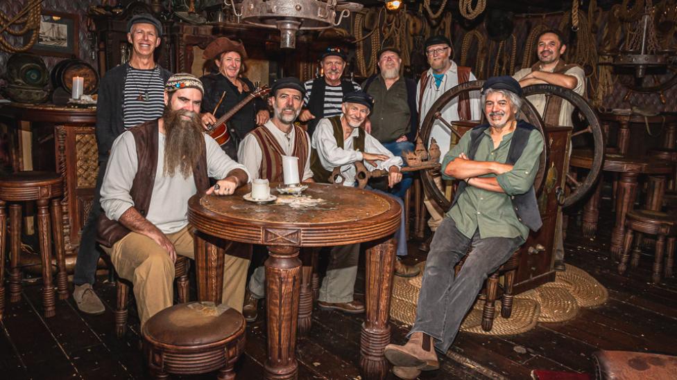 A folk band wearing seafaring clothes pose in a sailing-themed pub