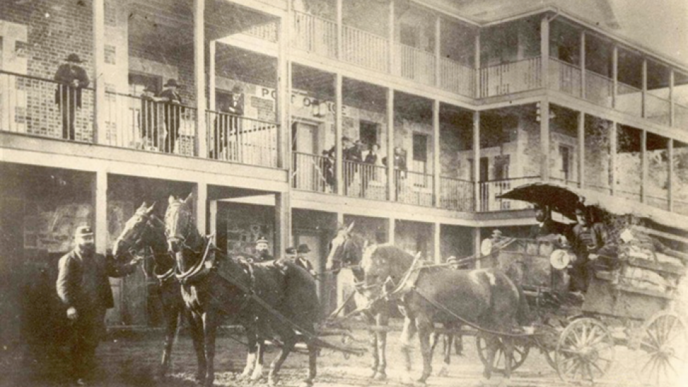 A sepia toned photograph of a horse-drawn carriage in front of a post office