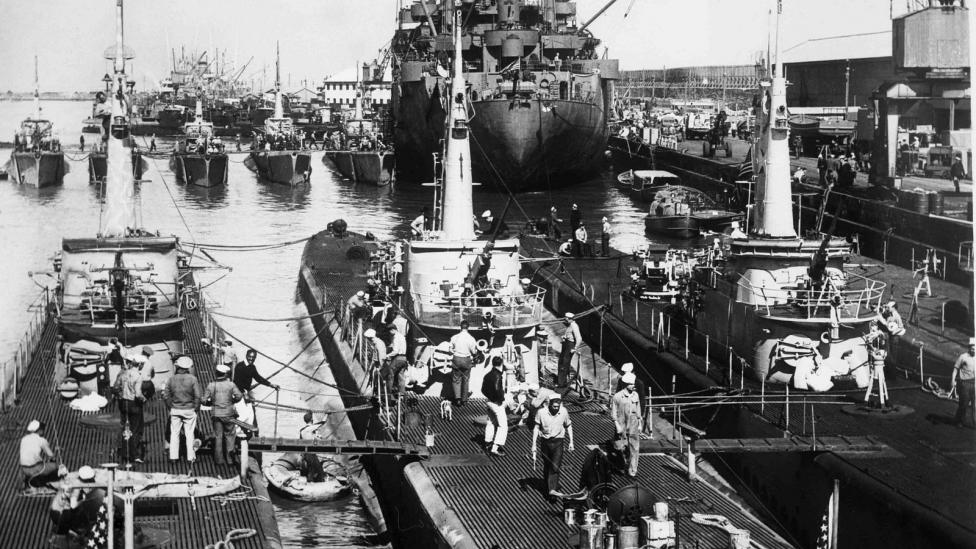 Black and white image of submarines and ships in dock