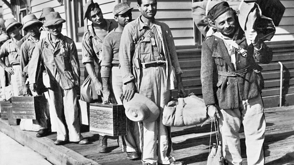 Italian prisoners of war carrying their their luggage wait to board a train bound for an Australian camp in 1943