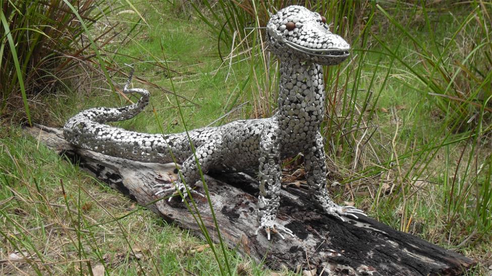 Stainless steel sculpture of a goanna perched on some decaying timber