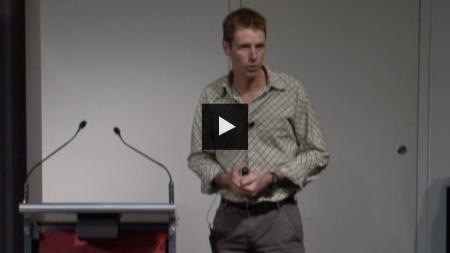 Glenn Moore stands at a podium, presenting a lecture